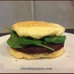 A sandwich with leafy greens and a patty between two flat pieces of bread is placed on a plate. The background has a tiled wall. The text "chachingqueen.com" is visible at the bottom, hinting at their delicious cloud bread recipe.