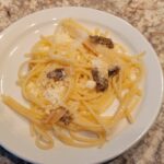 A plate of spaghetti with grated cheese and small truffle pieces on a marble countertop.