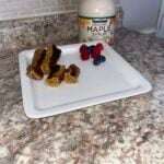A plate with French toast sticks and berries on a marble countertop. A bottle of organic maple syrup is in the background.