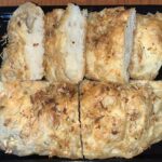 A rectangular tray with pieces of rosemary and onion focaccia bread.