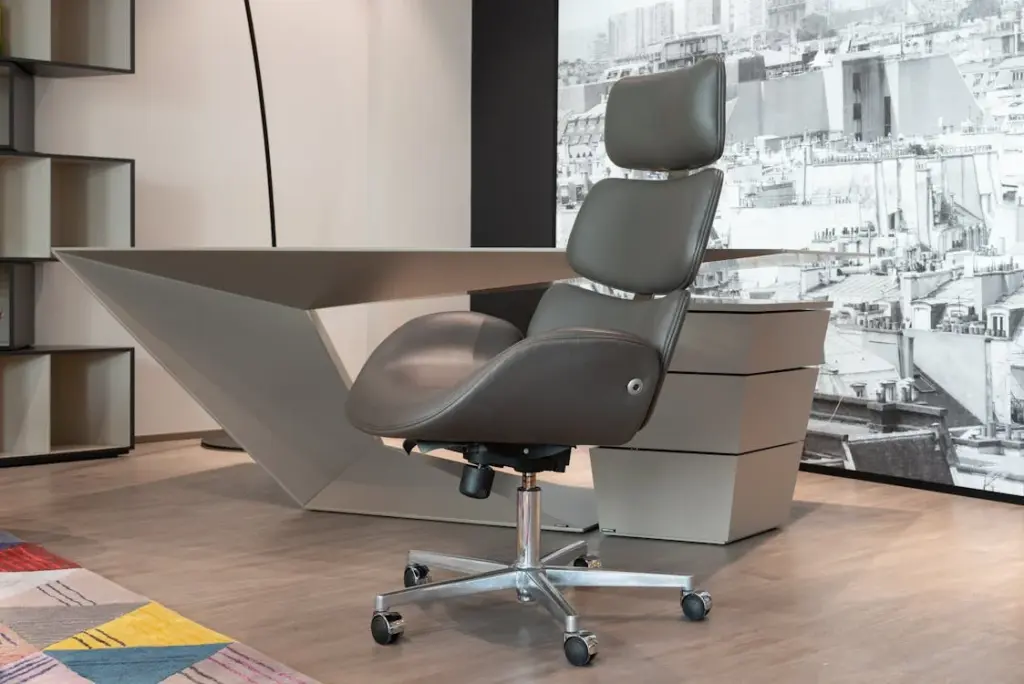 Modern office chair on wheels in front of a sleek, angular desk and shelves. Black-and-white mural in the background. Multicolored rug on wooden floor.