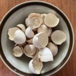A bowl filled with broken eggshells on a wooden surface.