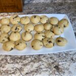 A white rectangular plate with 23 chocolate chip cookies on a marble countertop.