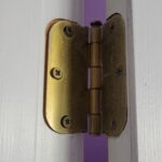 A metal hinge attaches a partially open white door to its frame.
