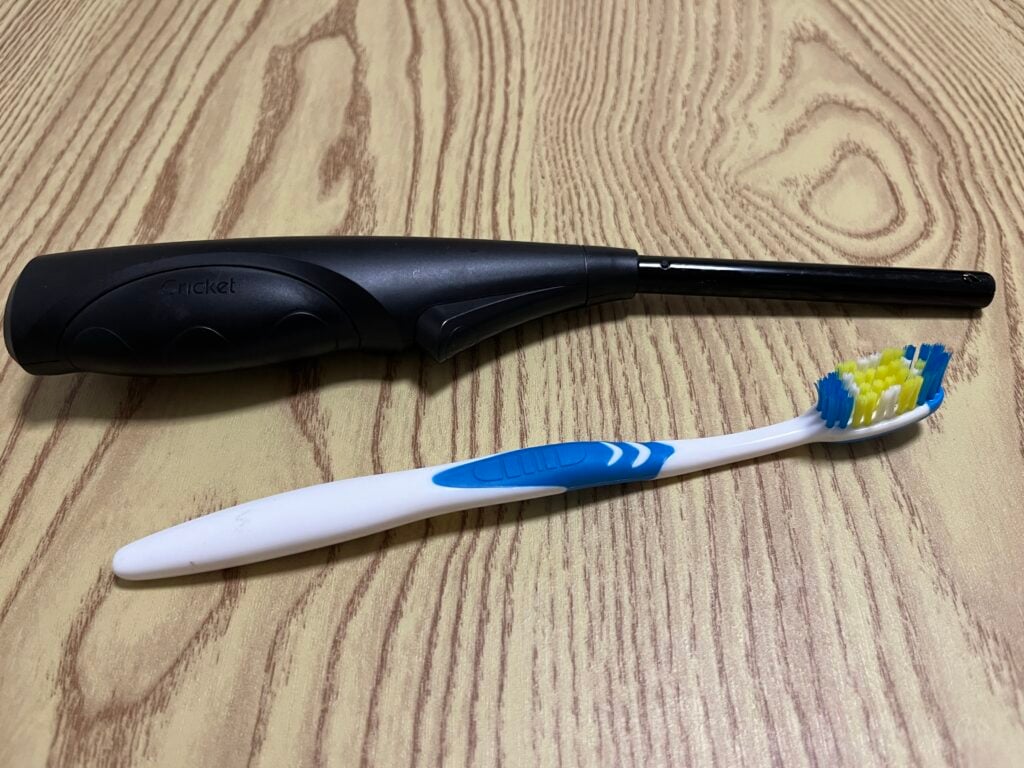 A black utility lighter and a blue-and-white toothbrush placed parallel on a light wood surface.