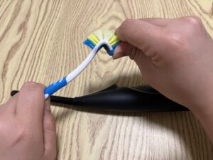 A person bends the neck of a blue and white toothbrush with both hands over a wooden surface.