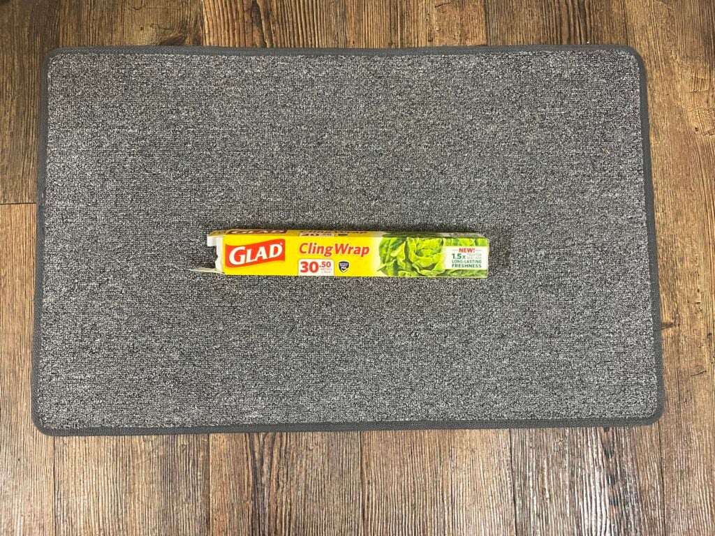A box of Glad Cling Wrap is placed on a gray mat, with a wooden floor in the background.