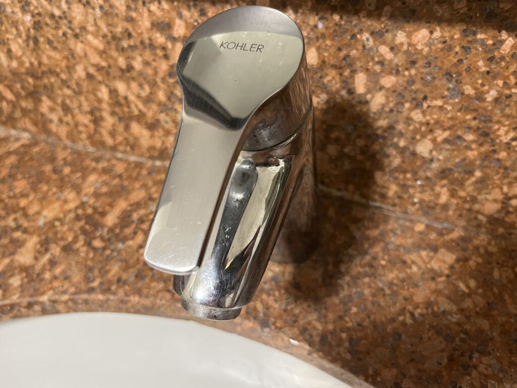 A close-up view of a chrome Kohler sink faucet with a textured brown countertop background.