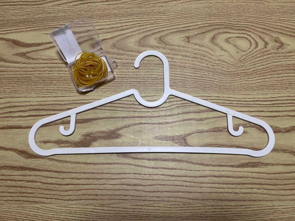 A white plastic hanger and an open plastic box filled with yellow rubber bands are placed on a wooden surface.