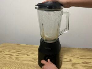 A person holds the lid and turns the dial of a Kyowa blender mixing a white liquid on a wooden table.