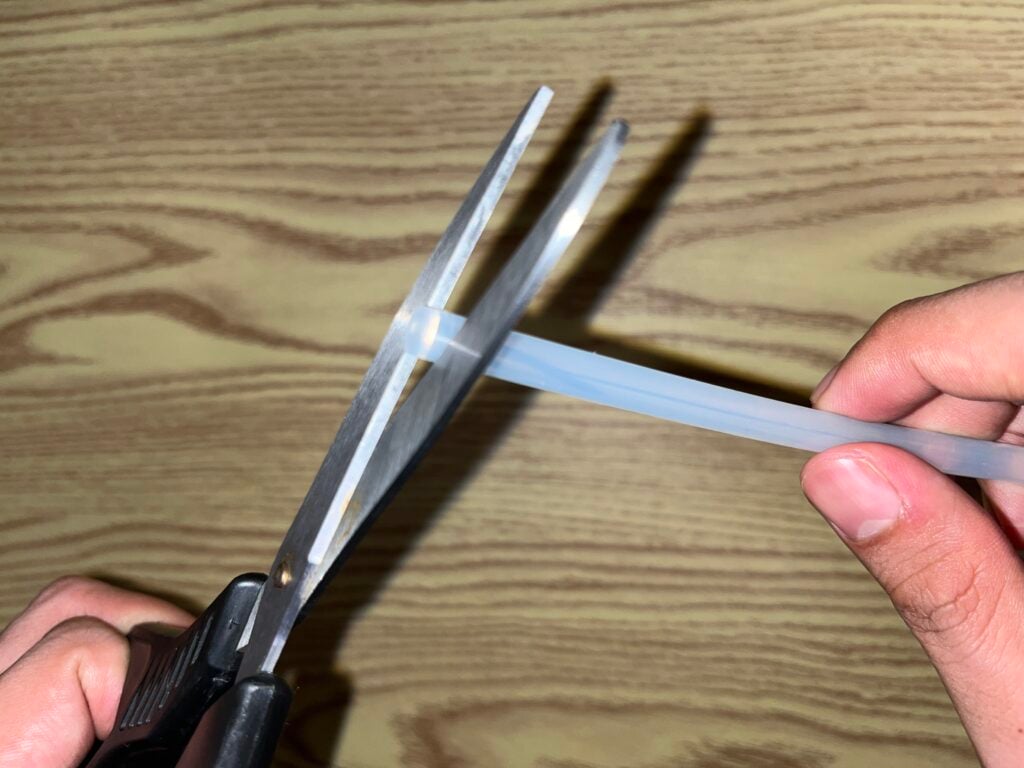 A person is using scissors to cut a transparent plastic zip tie against a wood-patterned background.