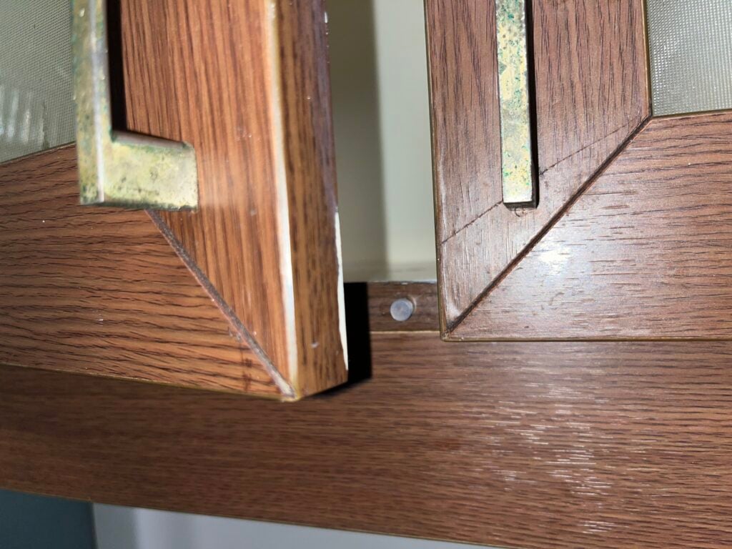 Close-up of two misaligned wooden cabinet doors with metal handles, showing a visible gap and a nail beneath one edge.