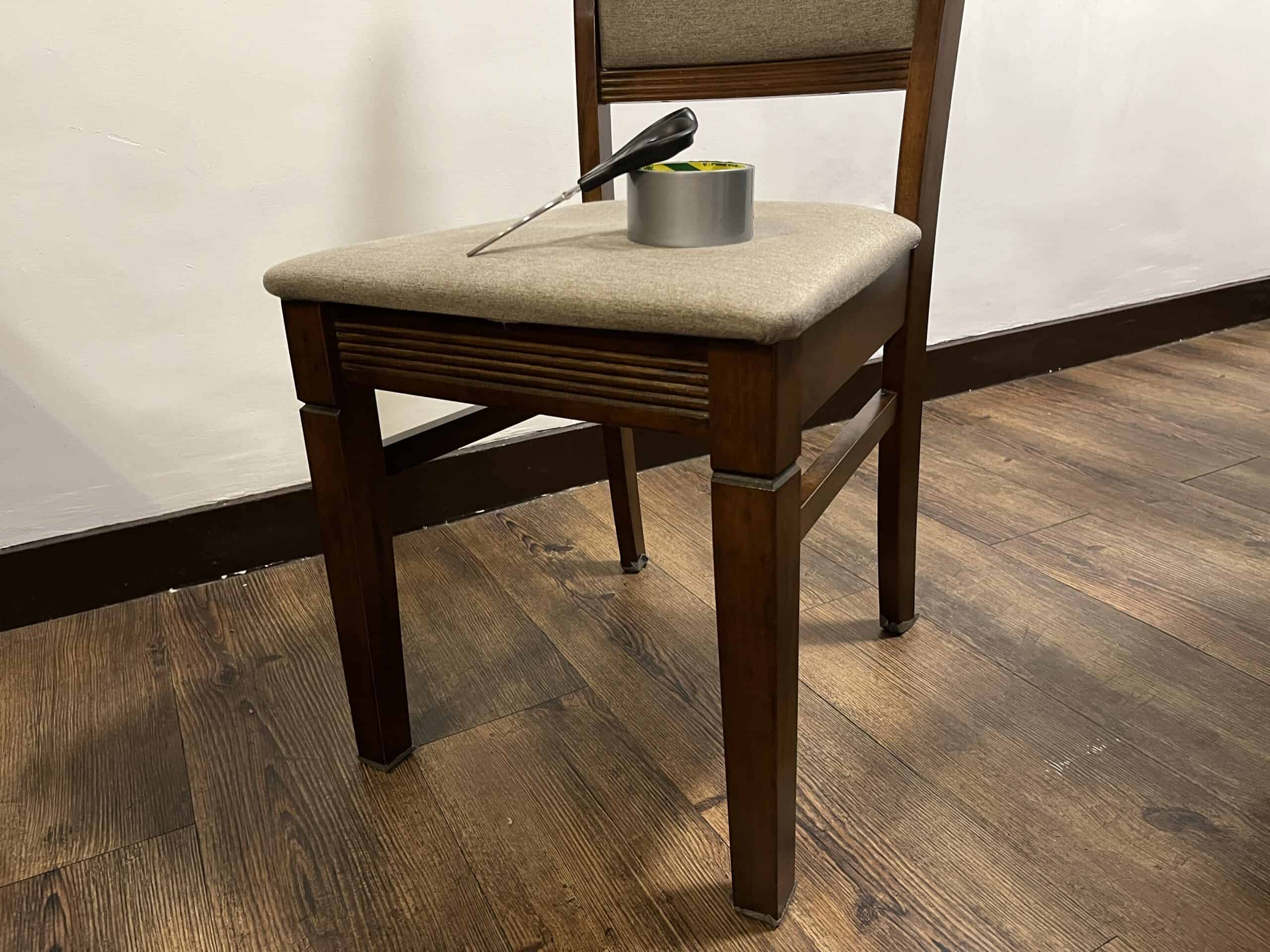 A pair of scissors and a roll of duct tape sitting on a wooden chair.