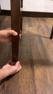 Hands attaching a clear floor protector to the bottom of a wooden chair leg.