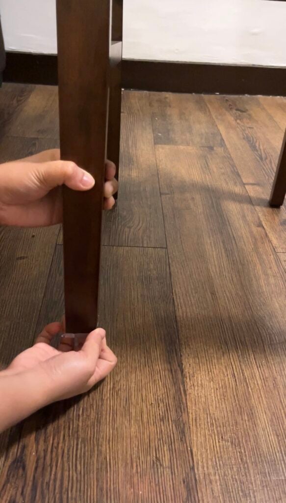 Hands attaching a clear floor protector to the bottom of a wooden chair leg.