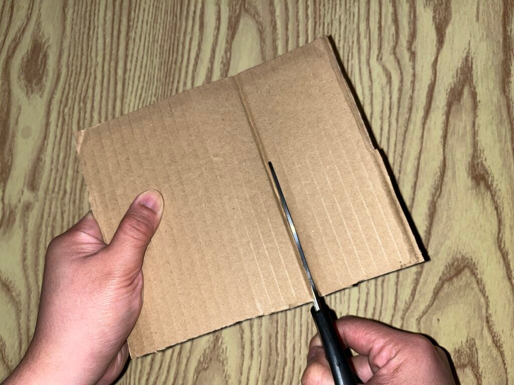 Hands using scissors to cut a piece of cardboard.